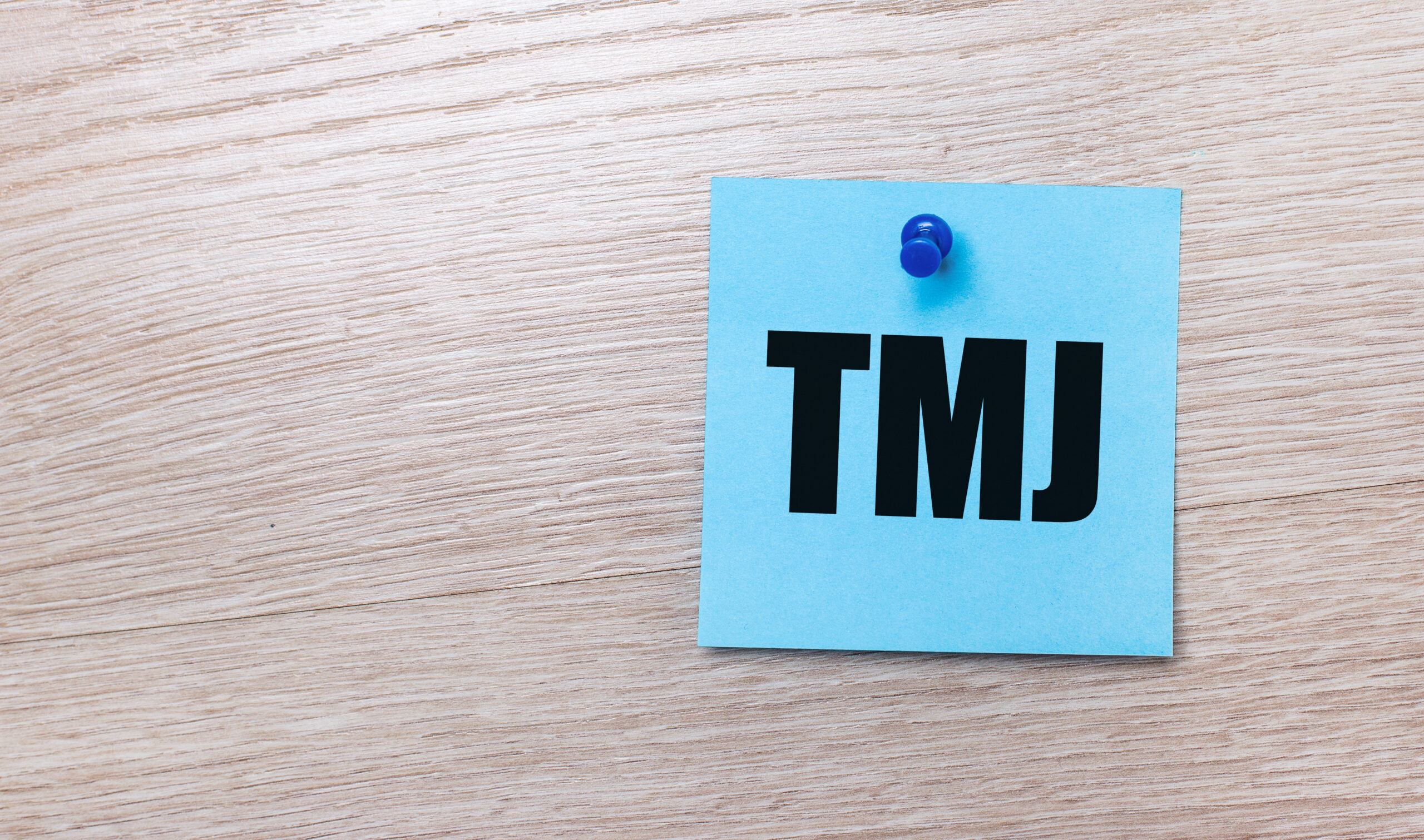 On a light wooden background - a light blue square sticker with the text TMJ