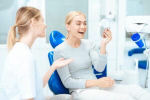 A woman is sitting at a dentist's reception. She looks in the mirror at her teeth. A dentist is sitting next to each other. Woman smiling